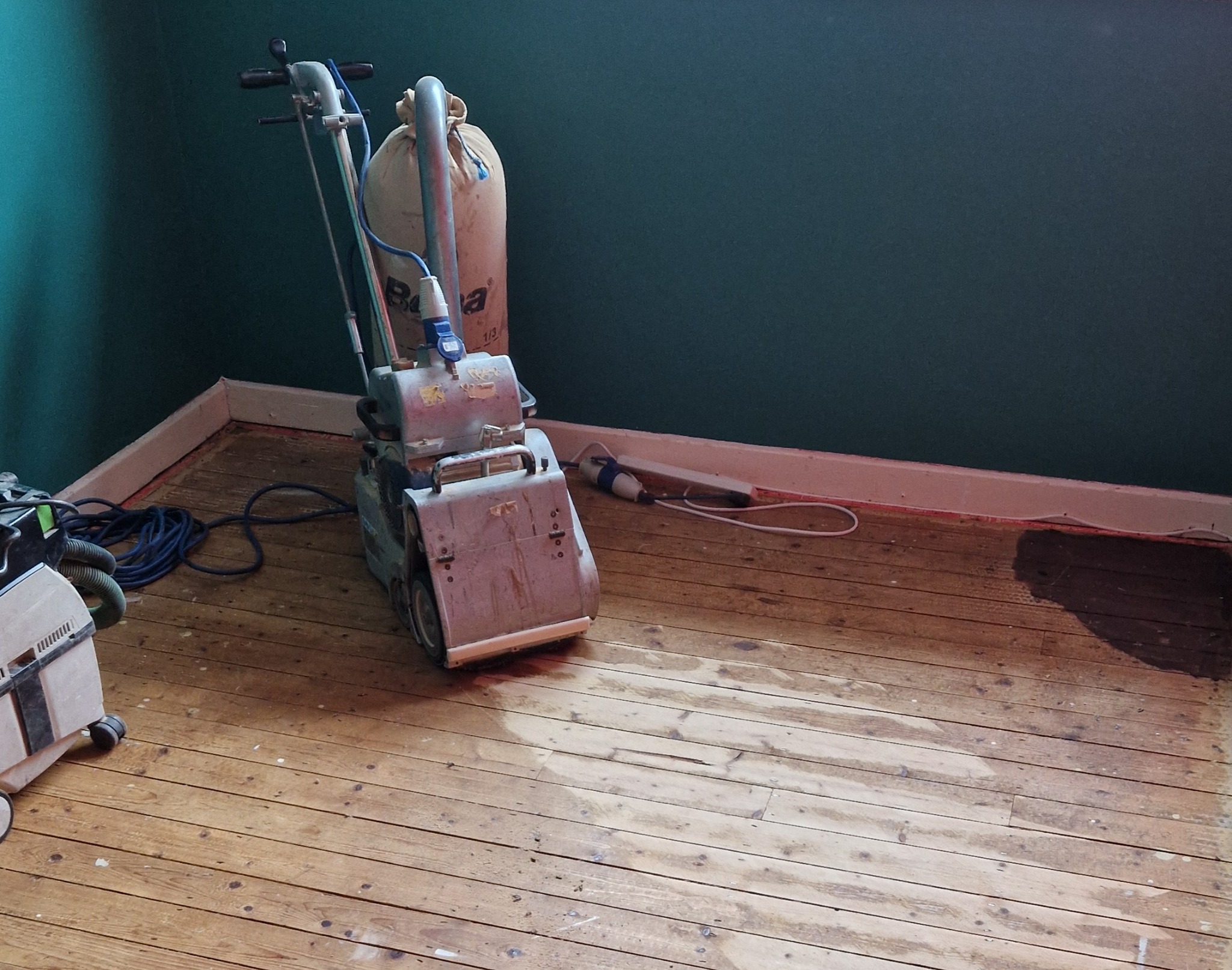 Industrial belt floor sander resting on partially sanded Victorian pine floorboards in an Anerley home, revealing the transformation to Beautifully Sanded Floors.