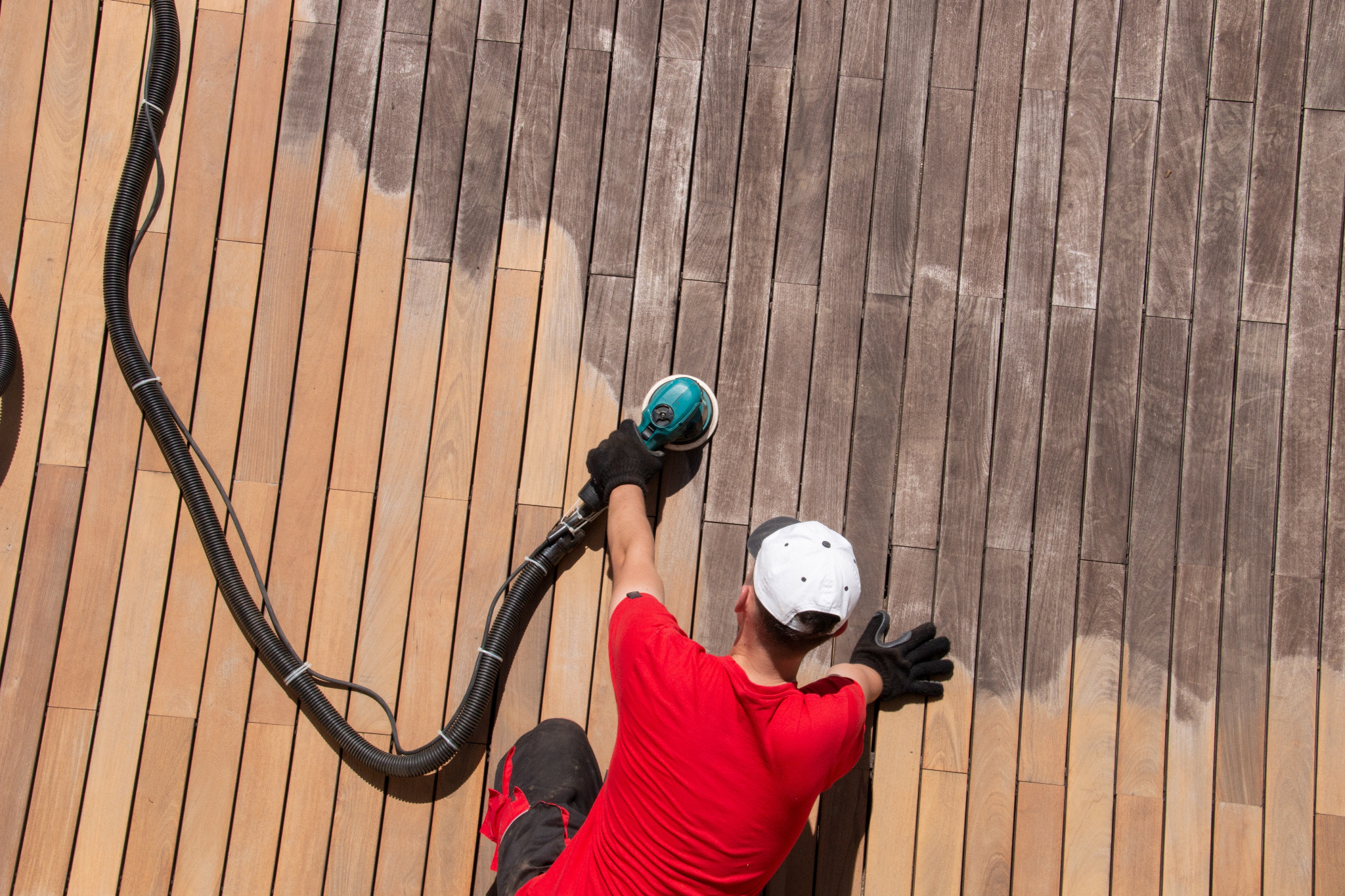 Deck Sanding Grits in Anerley – technician using a dust-extracted random-orbital sander to remove greying and raised grain from a teak hardwood deck, revealing clean timber.